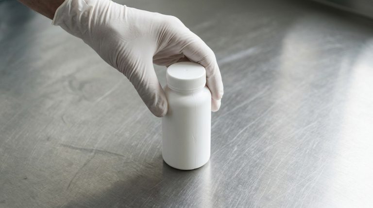 Gloved hand handling a food supplement bottle in a pharmaceutical manufacturing environment – Noviatic.